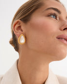 Los pendientes Pearl, inspirados en los elegantes collares de perlas de la era del jazz, combinan lujo y modernidad. Fabricados en plata de ley 925 con un baño de oro amarillo de 18 quilates, estos pendientes destacan por su delicada perla de nácar en talla gota como piedra principal. Con una longitud de 30 mm y cierre de tuerca, son perfectos para quienes buscan una pieza sofisticada y atemporal, ideal para destacar en cualquier evento.